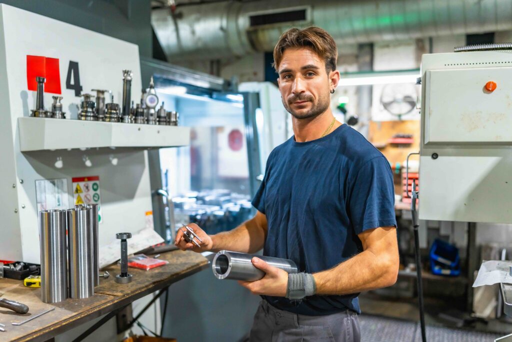Een verspaner. Een man met een metalen object in zijn hand in de werkplaats